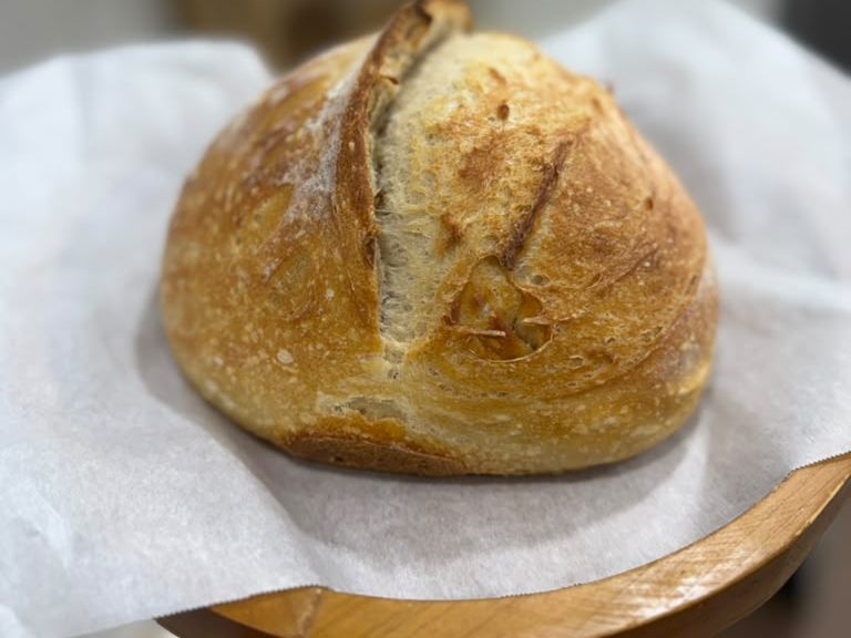 A round sourdough loaf with a deep score, resting on parchment